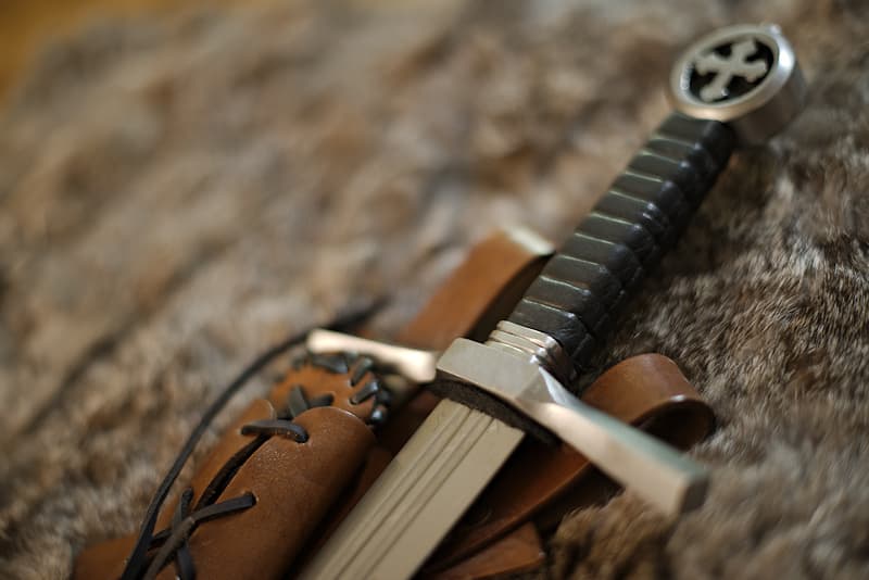 Combat dagger with trefoil cross pommel and laced brown leather scabbard, slanting.