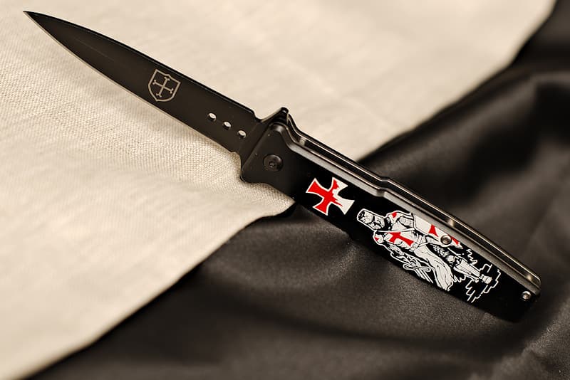 Stainless steel and metal folding knife, screen-printed with a Templar on the handle and engraved with a Templar coat of arms on the blade, delivered in a metal case decorated with knights and the Templar motto "Non nobis Domine, non nobis, sed Nomini Tuo da Gloriam" | The box in which I'm discreetly stored bears the Latin inscription "Non nobis Domine, non nobis, sed Nomini Tuo da Gloriam", meaning "Not for us Lord, not for us, but in your name and for your glory".