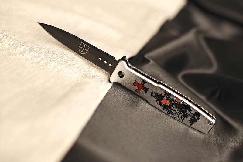 Stainless steel and metal folding knife, screen-printed with a Templar on the handle and engraved with a Templar coat of arms on the blade, delivered in a metal case decorated with knights and the Templar motto "Non nobis Domine, non nobis, sed Nomini Tuo da Gloriam" | My name comes from the Provençal - and Old French - "bausan". This term refers to a balzan horse: black, with white spots above the hoof. This is the true origin of the word for the Templar knight's standard, the beaucéant.