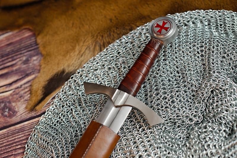 Forged medieval sword, circular pommel with red Templar cross, throat blade, brown and black leather scabbard with adjustable shoulder strap.