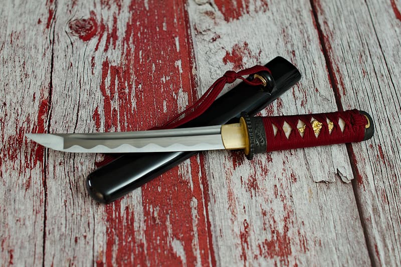 Tantō sharp, damascened forge, with black scabbard (saya 鞘), tsuka-ito (柄糸) and dark red sageo (下緒), delivered in a wooden case, with a protective cloth cover | Although I was forged after my two big sisters, the katana and wakizashi blades, I convey the same symbolism of fairness, dear to our samurai master.