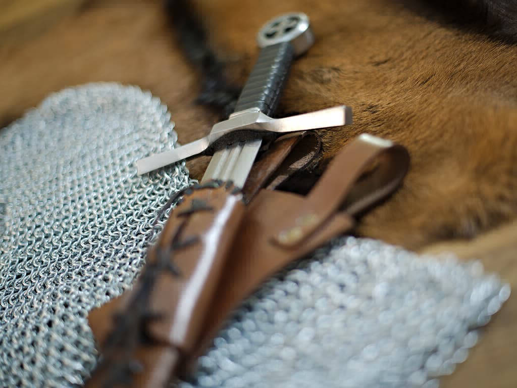Épée médiévale du chevalier croisé posée sur une peau naturelle, une table et une cotte de mailles médiévale Épée médiévale du chevalier croisé posée sur une peau naturelle, une table et une cotte de mailles médiévale