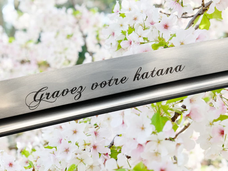 Laser engraving on the blade of a katana: the phrase "Gravrz votre katana" (Engrave your katana) in a pretty untied carcatère font #Terressens
