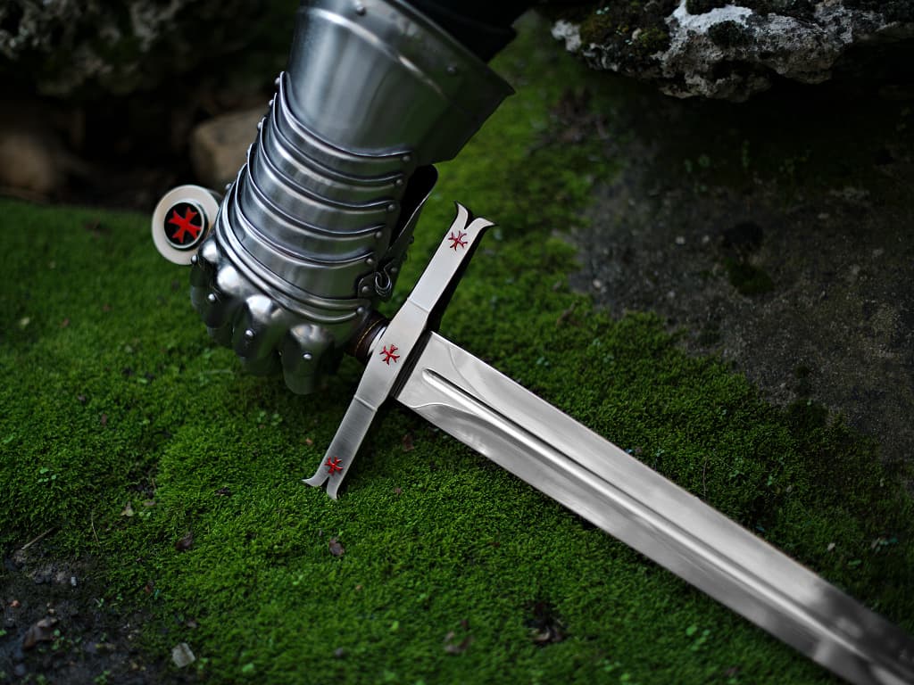 A hand protected by a medieval gauntlet takes possession of the decorative Templar sword. A hand protected by a medieval gauntlet takes possession of the decorative Templar sword.
