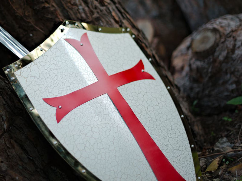 Decorative Templar shield on a wooden background, with a Templar sword in the background. Decorative Templar shield on a wooden background, with a Templar sword in the background.