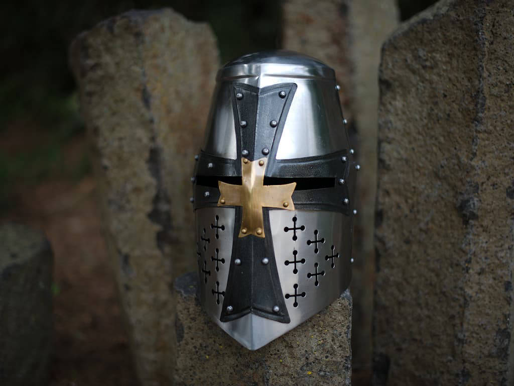 Heaume templier en acier, croix noire et laiton posé sur des pierres Heaume templier en acier, croix noire et laiton posé sur des pierres